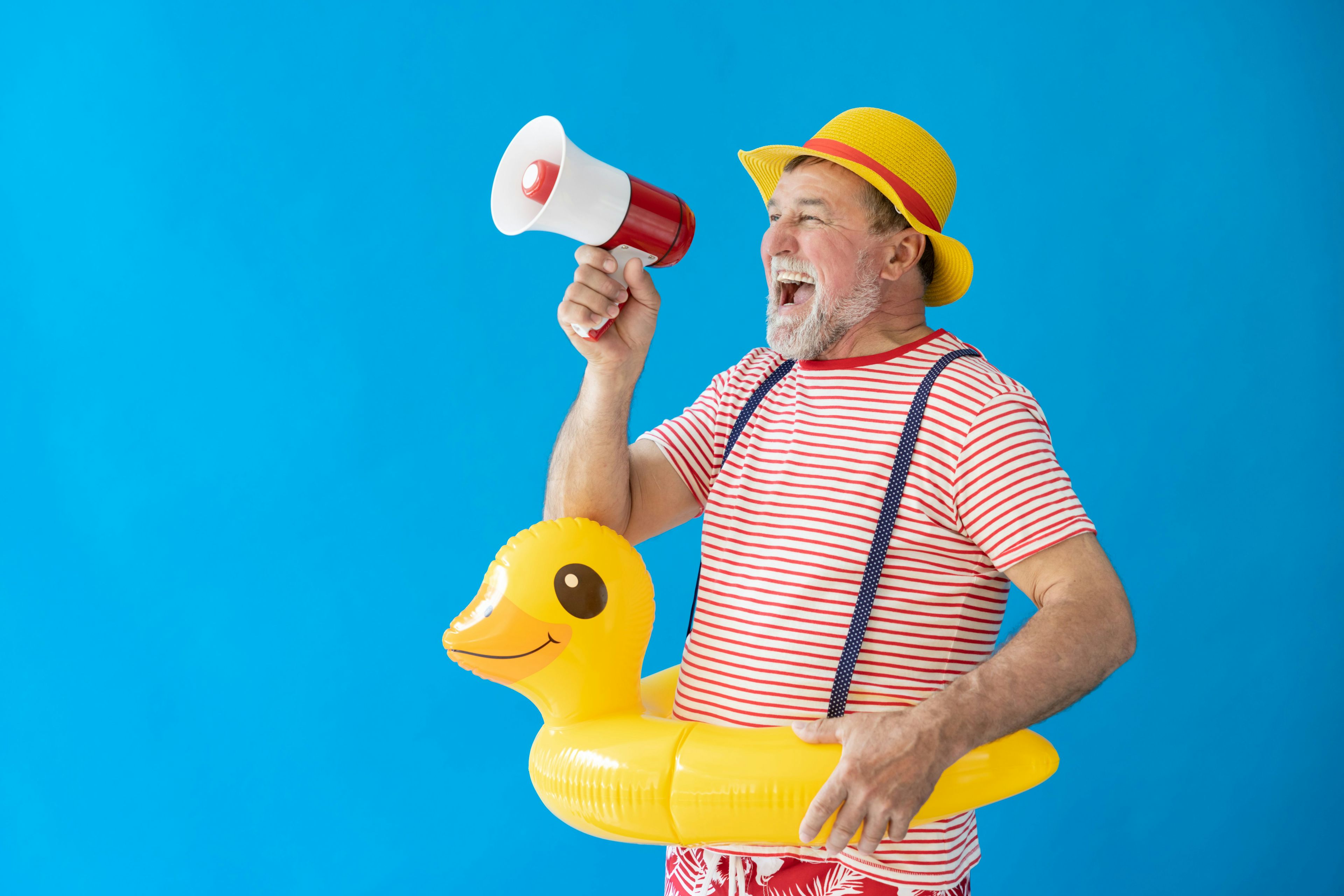 Ein älterer Mann mit Schwimmreif und Megaphon freut sich auf seine Sommerferien. 