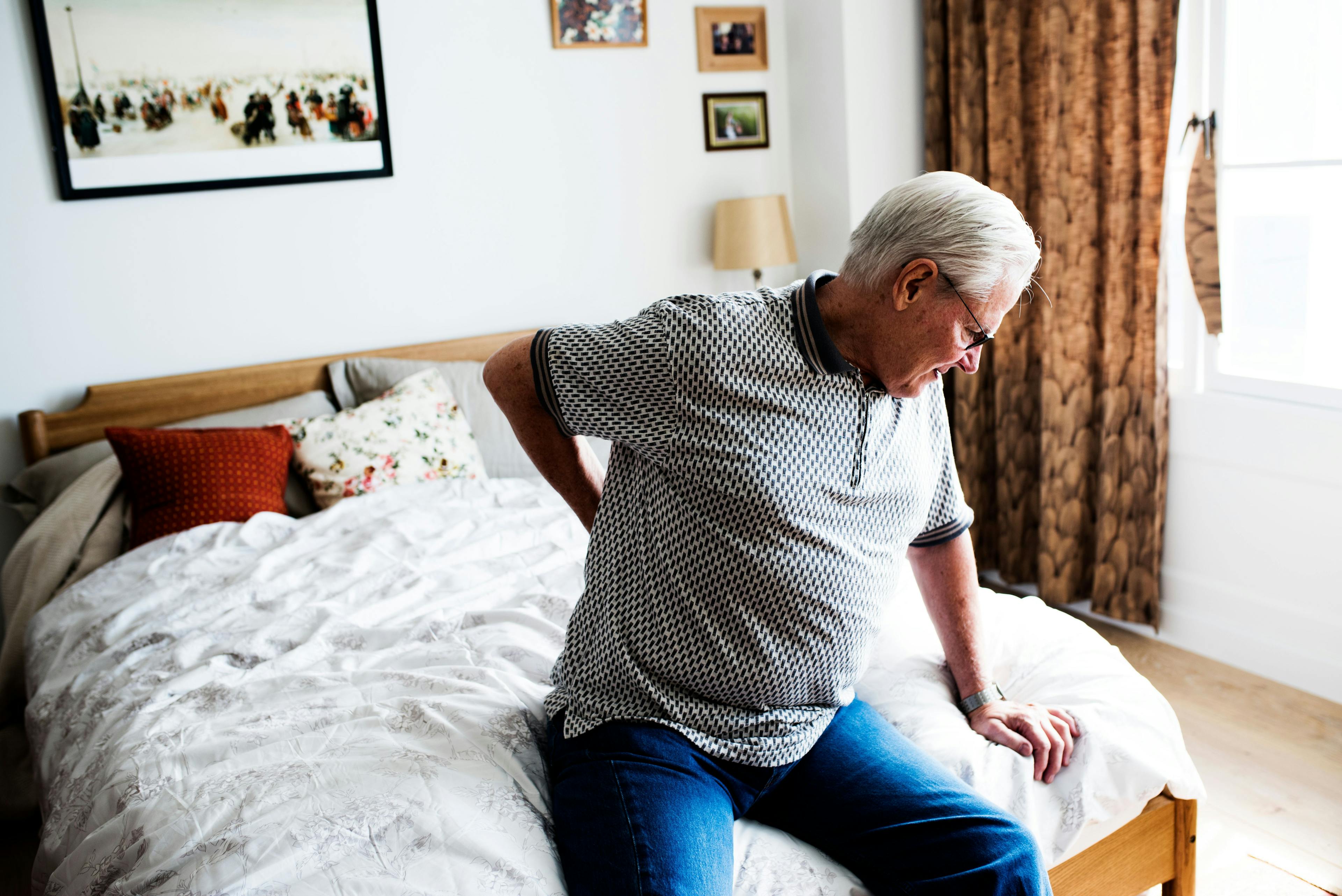 Ein Senior sitzt mit Schmerzen auf dem Bett. 